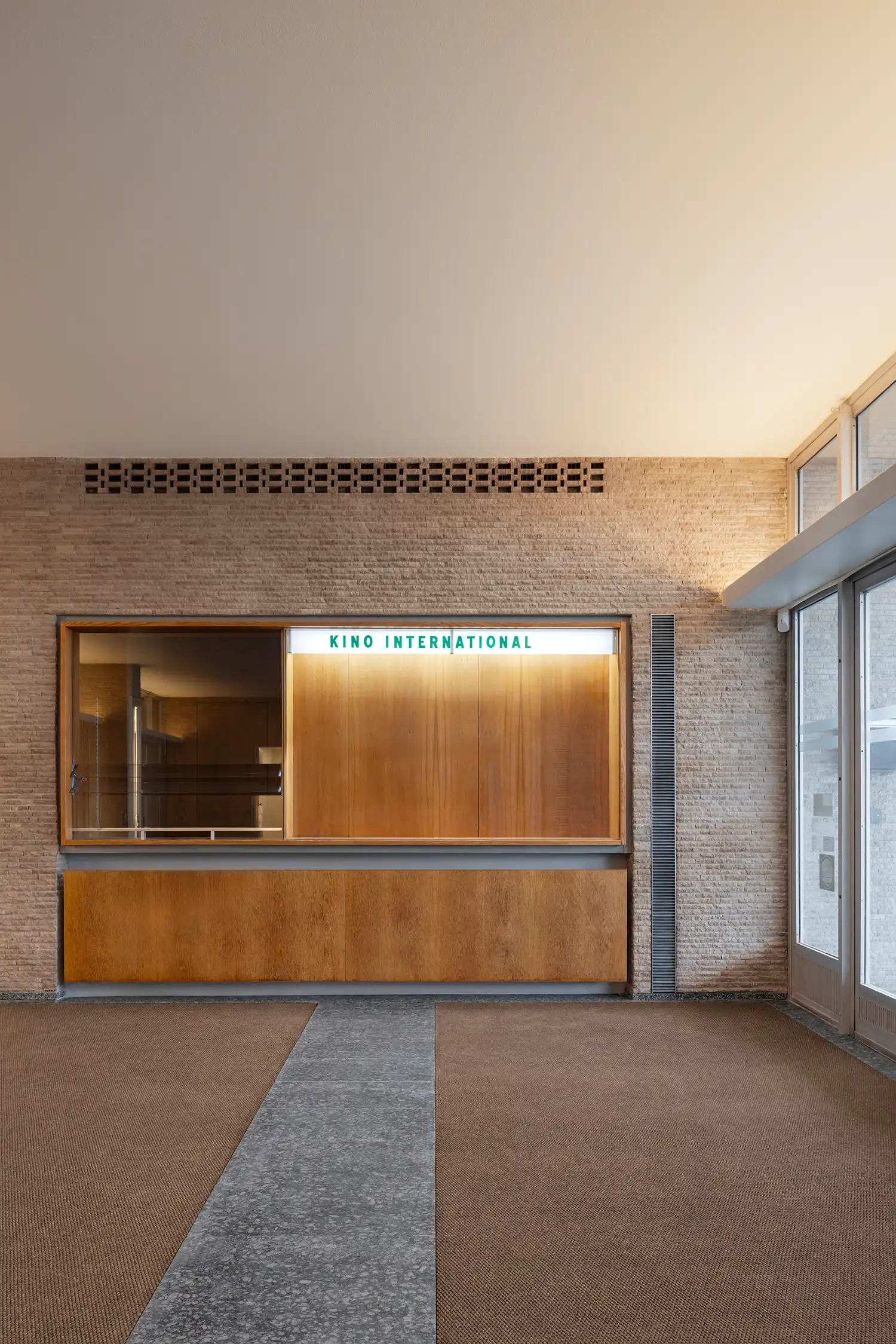 Minimalist wooden ticket counter set against a textured stone wall inside the cinema foyer.