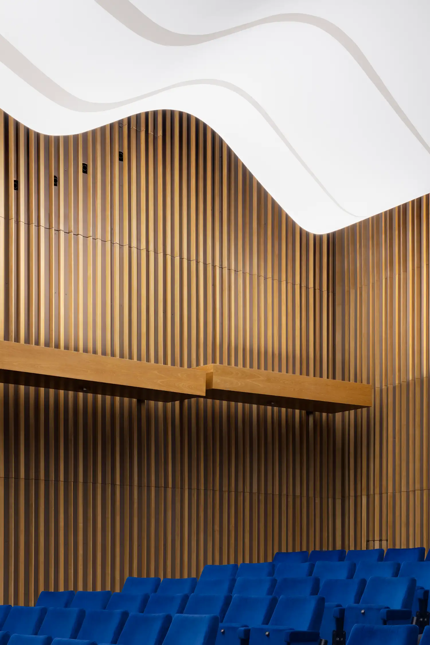 Close-up of vertical wooden slats in the auditorium under a flowing, wave-like white ceiling.