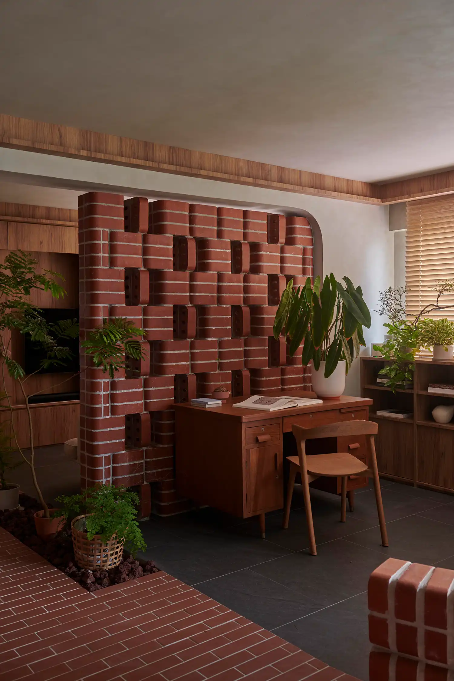 A wooden desk positioned against a tessellated red brick wall in a Singapore apartment.