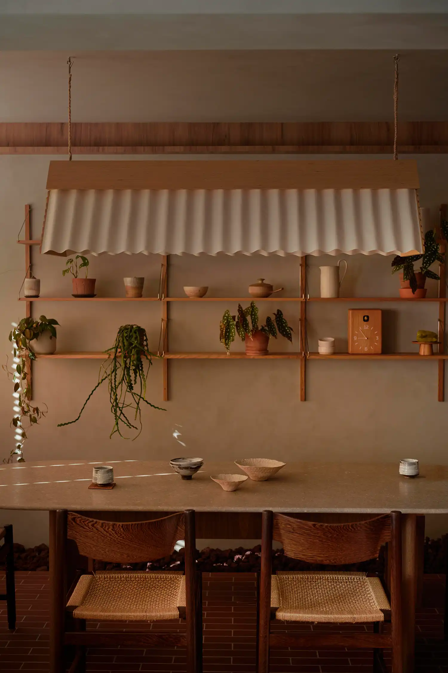 Minimalist dining area with a stone table, wooden chairs, and a corrugated pendant light.