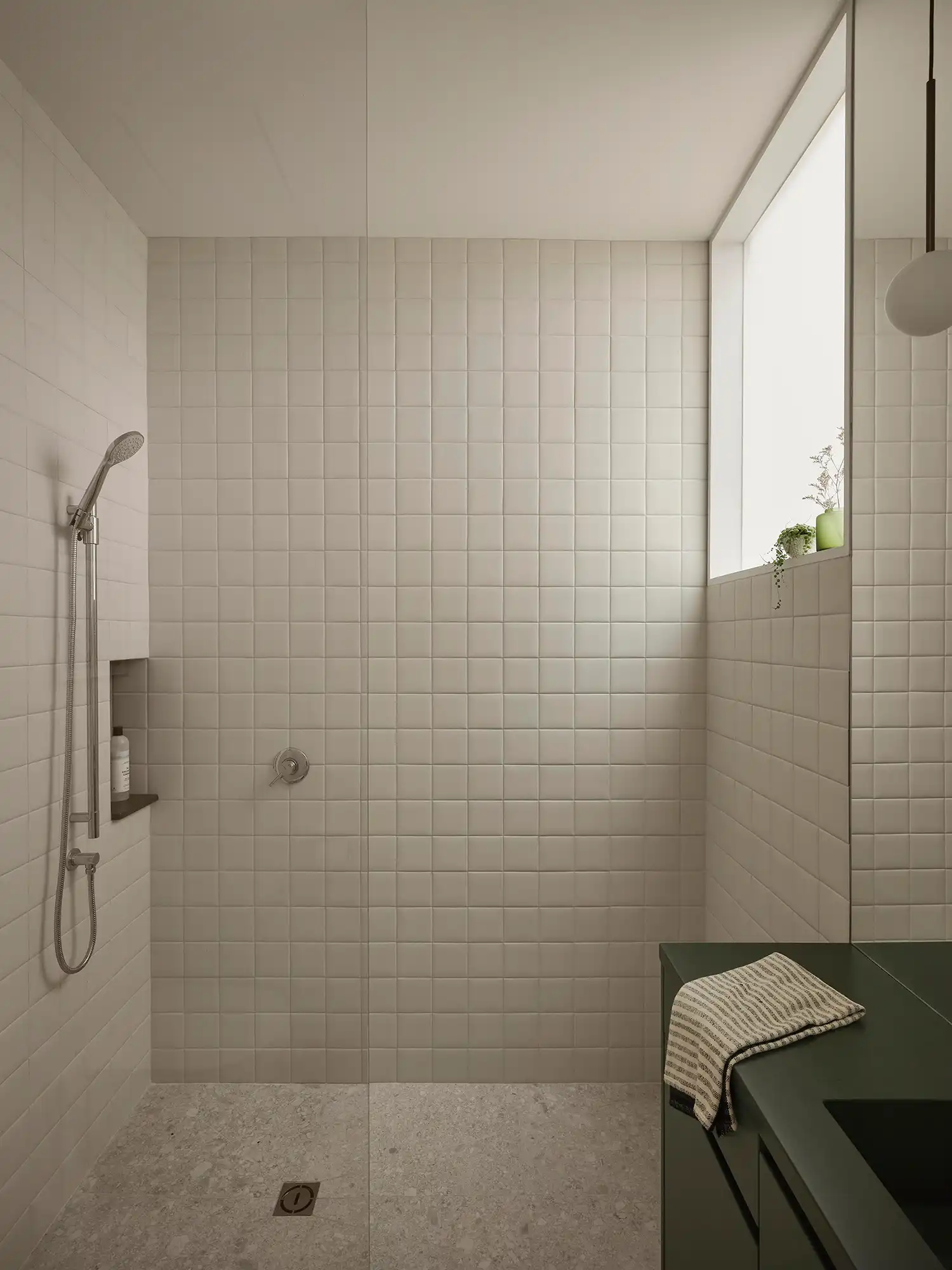 Minimalist bathroom with white square tiles, a dark green vanity, and a frosted interior window.