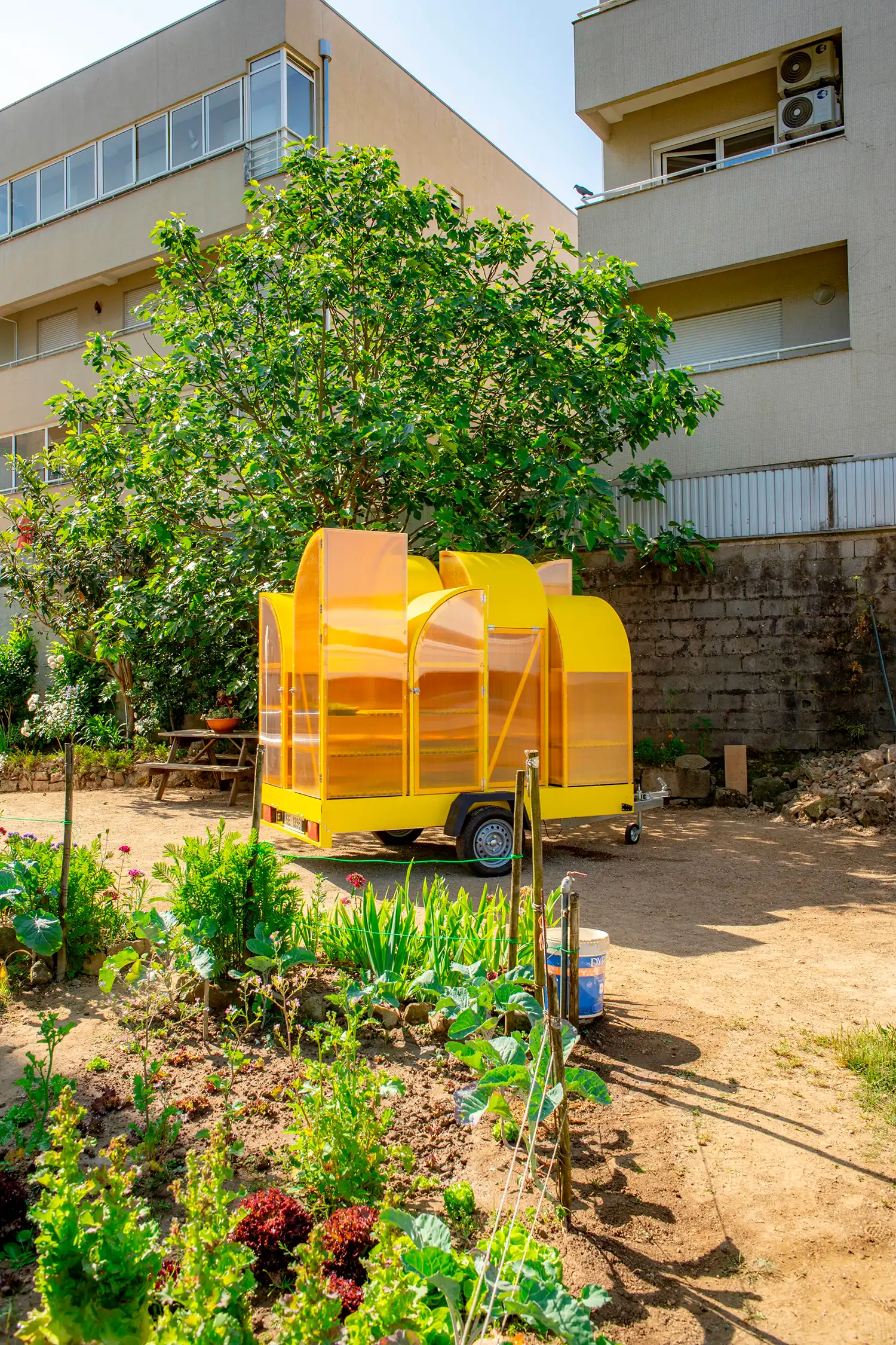 Modular yellow greenhouse on wheels positioned in an urban garden in Braga, Portugal.