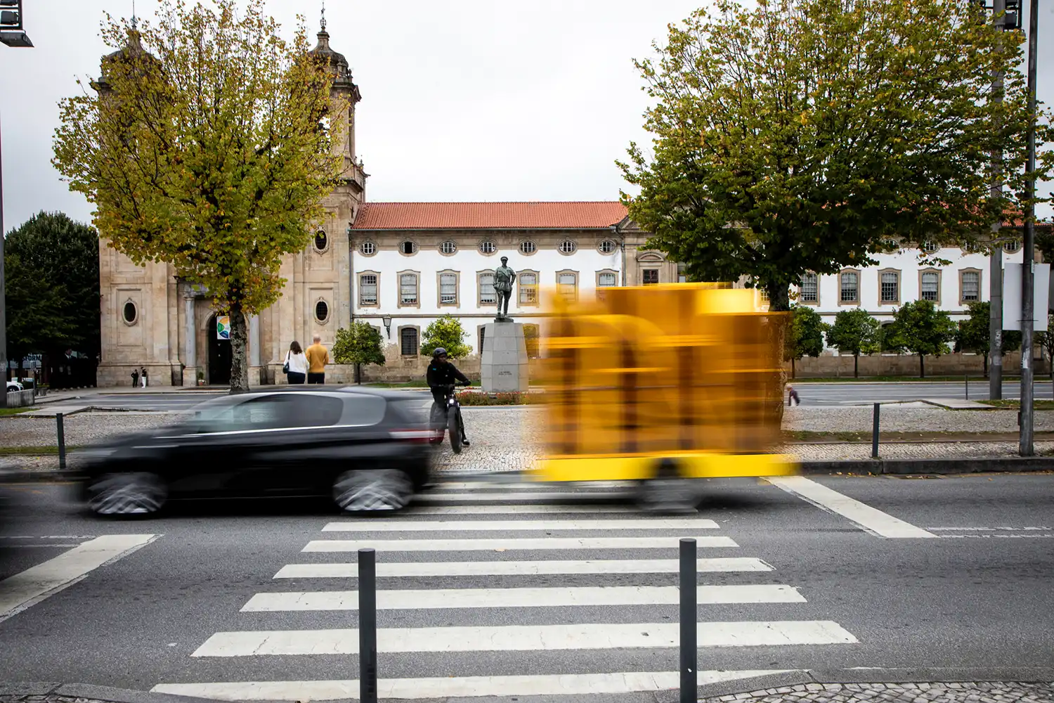 Motion blur of the yellow mobile seedbed crossing a city street in front of a historic building.
