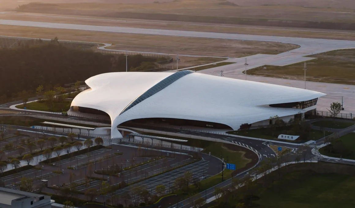 Aerial side view of MAD Architects' Lishui Airport terminal in Zhejiang with a fluid white roof at sunset.
