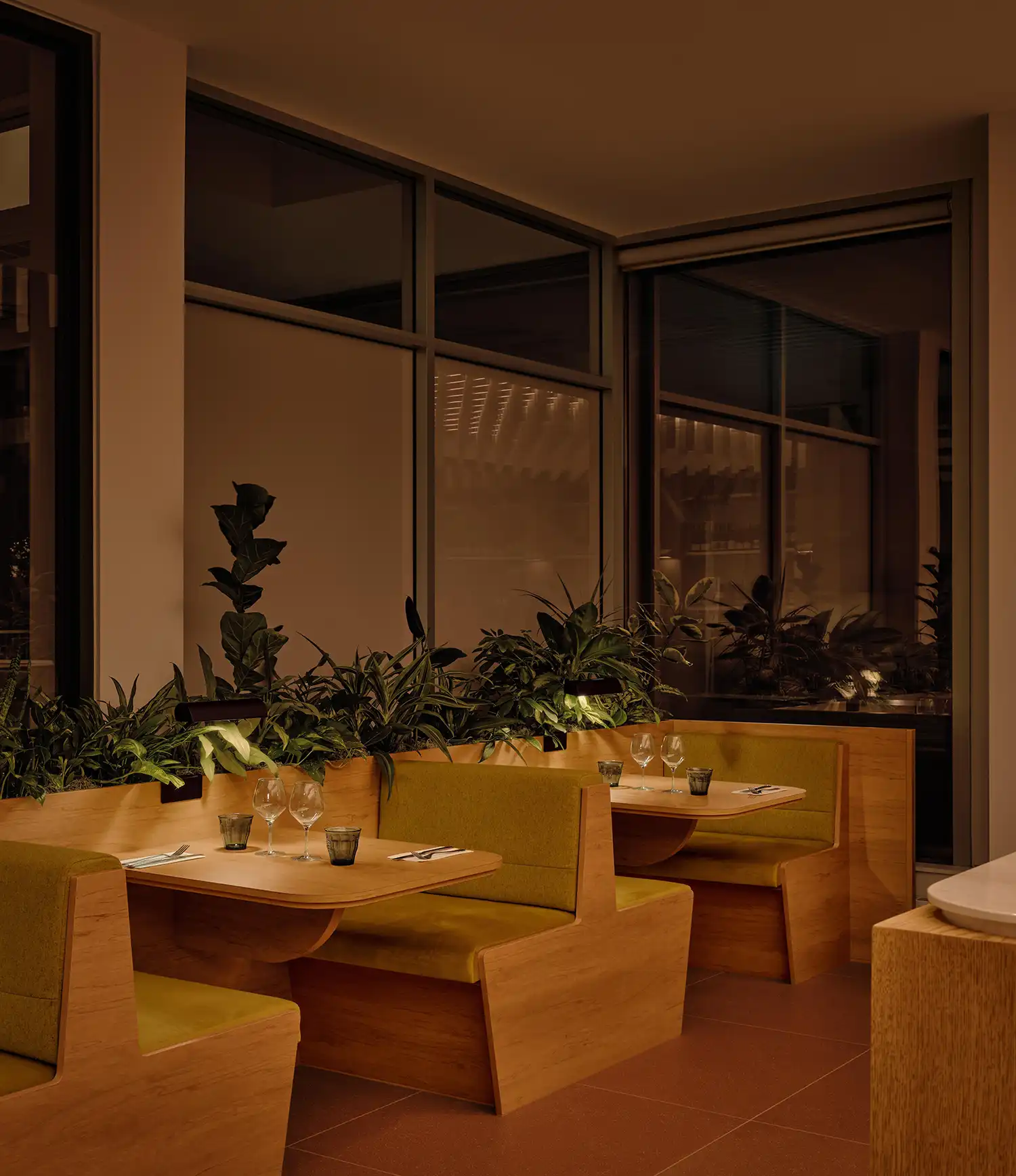 Intimate bistro booths in light wood with olive green upholstery and integrated planters