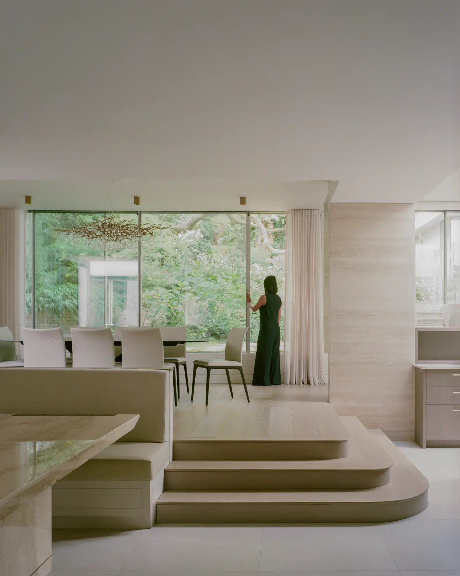 Interior dining room featuring a tiered floor level and a large window overlooking a terraced garden.