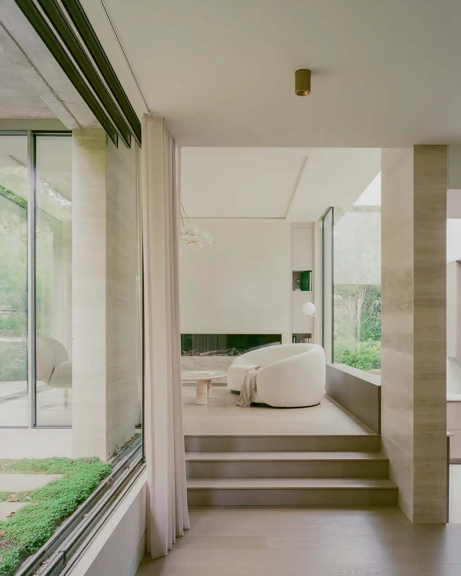 Sun-drenched lounge with minimalist white furniture and tiered floor levels leading to a garden view.