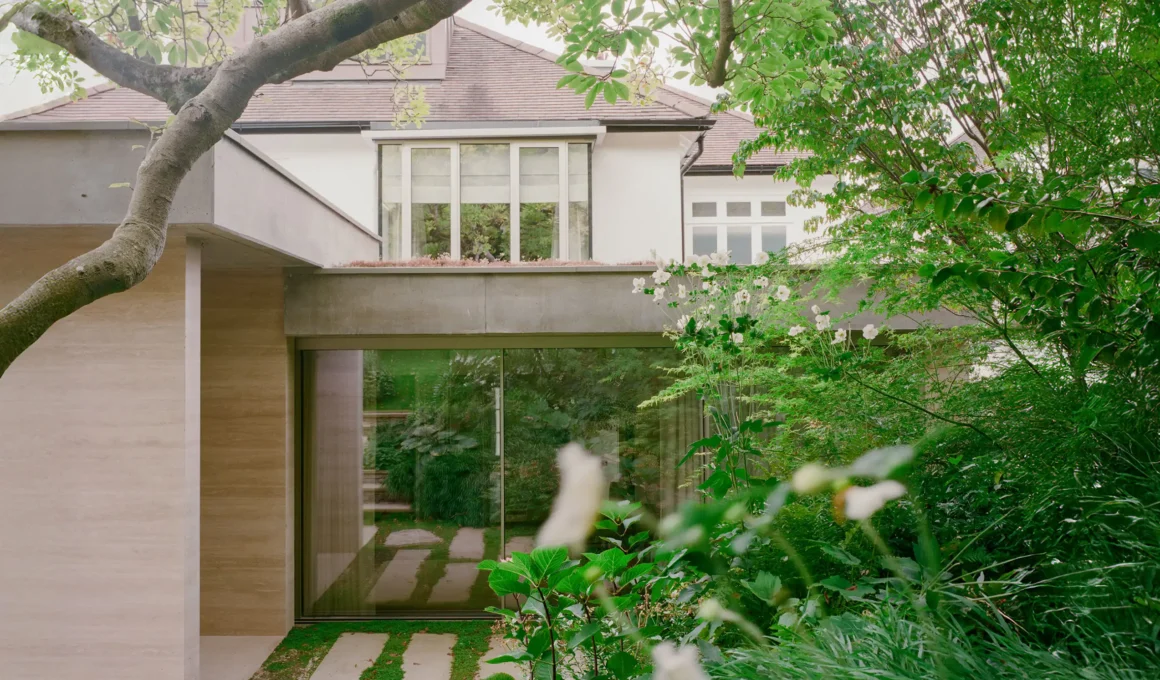 Travertine and concrete extension facade with a green roof overlooking a lush garden in Highgate, London.