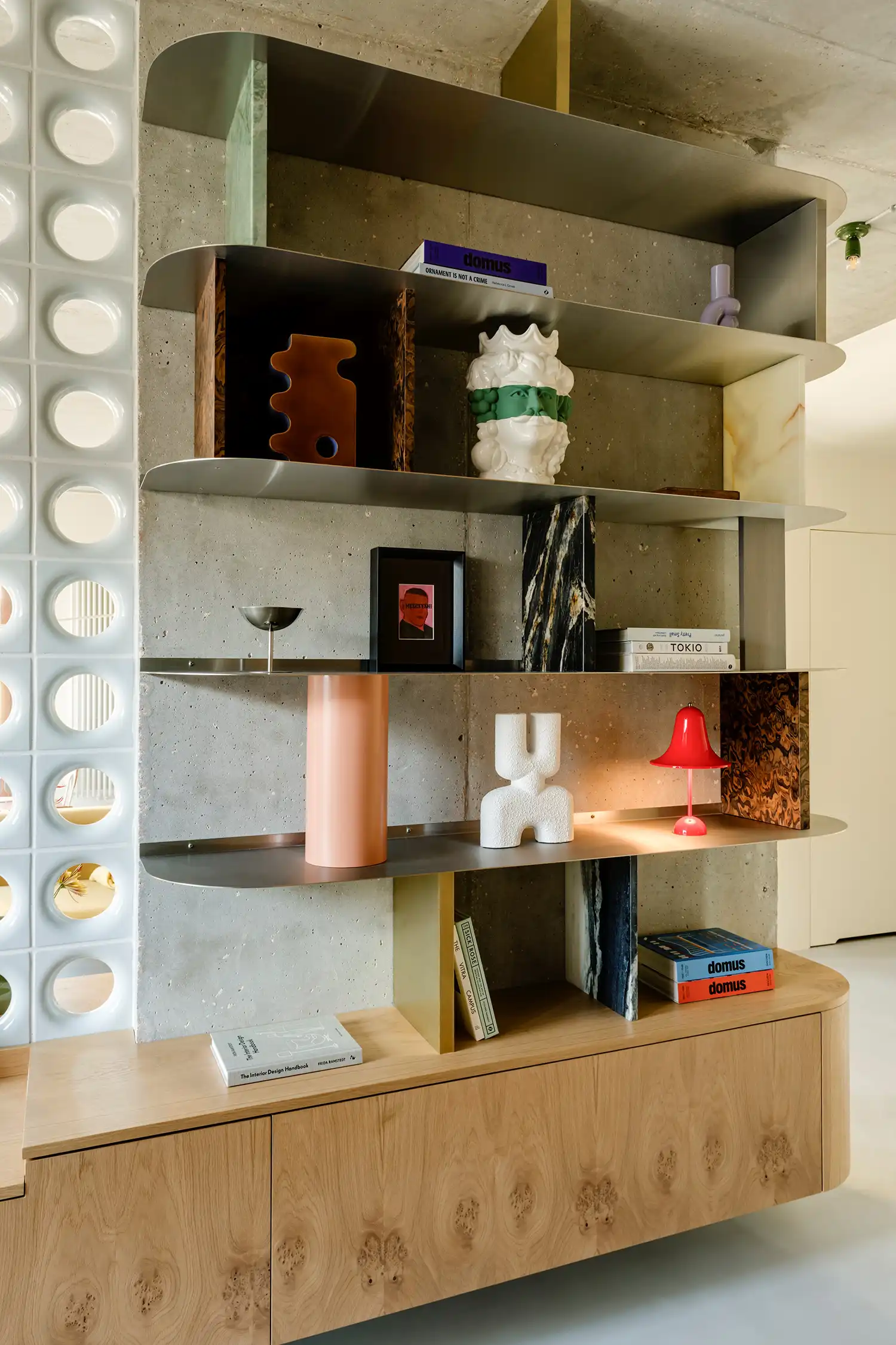 Custom metal bookshelf on concrete wall with red Artemide lamp