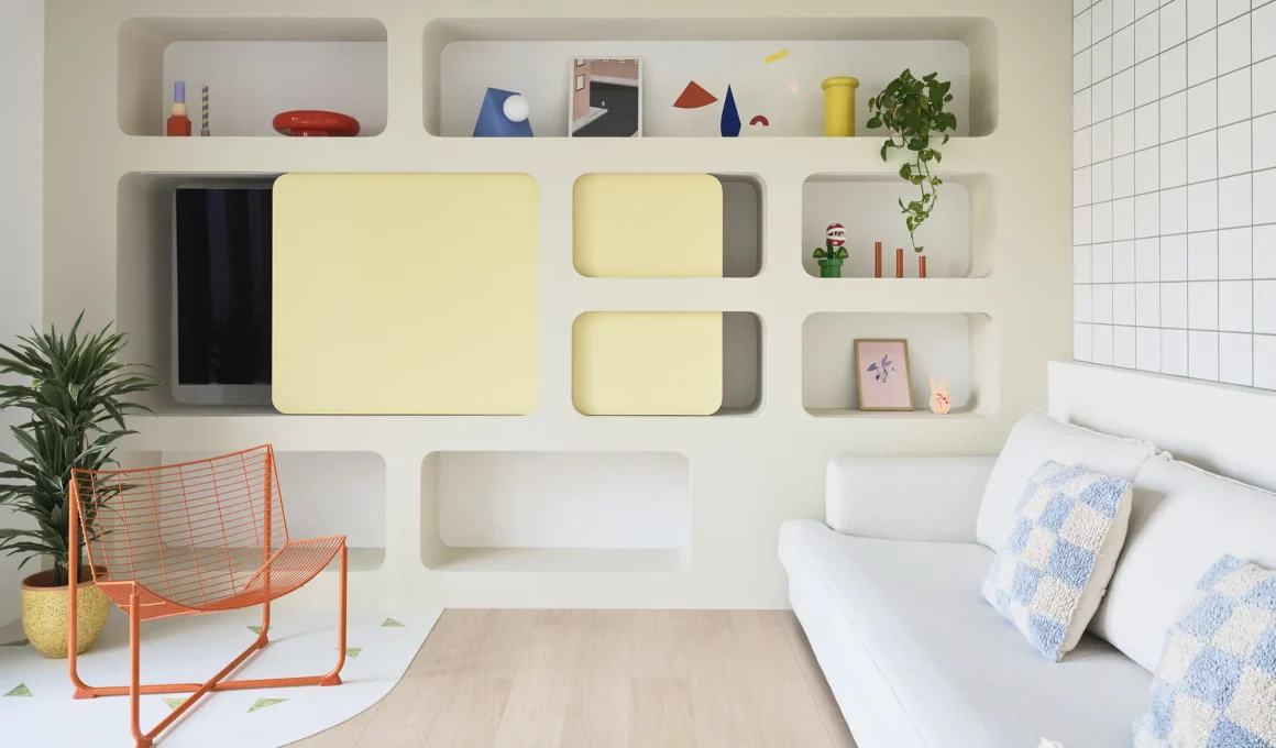 A neuroarchitectural living room featuring curved yellow niches, an orange wire chair, and lighting designed to boost serotonin and combat Seasonal Affective Disorder.