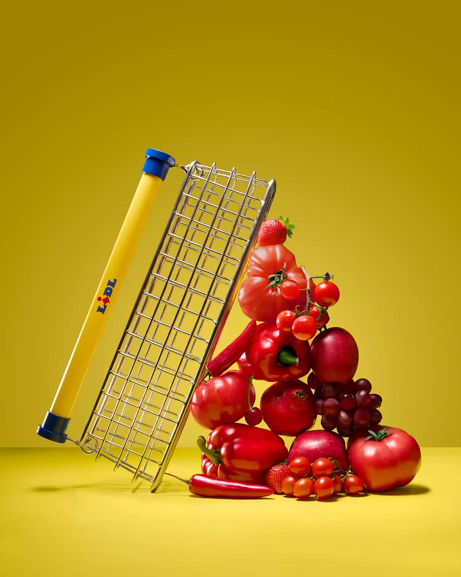 The Trolley Bag leaning against a vertical stack of red vegetables on a minimalist yellow background.