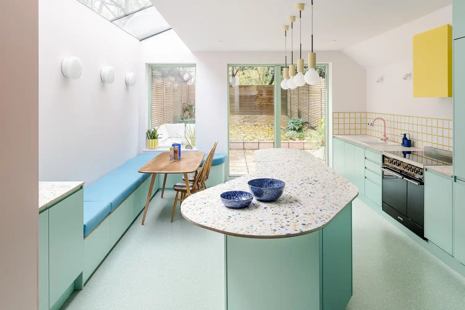 Bright kitchen with a large curved mint green island, terrazzo-style worktops, and a blue built-in banquette.