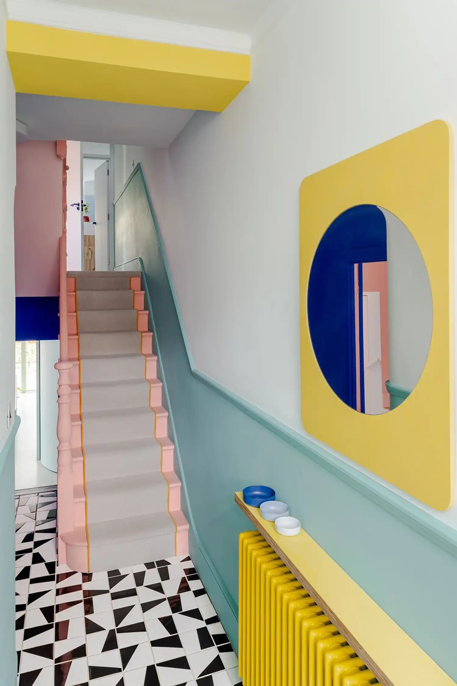 Staircase and hallway featuring a geometric black and white floor, teal wainscoting, and a yellow circular mirror.