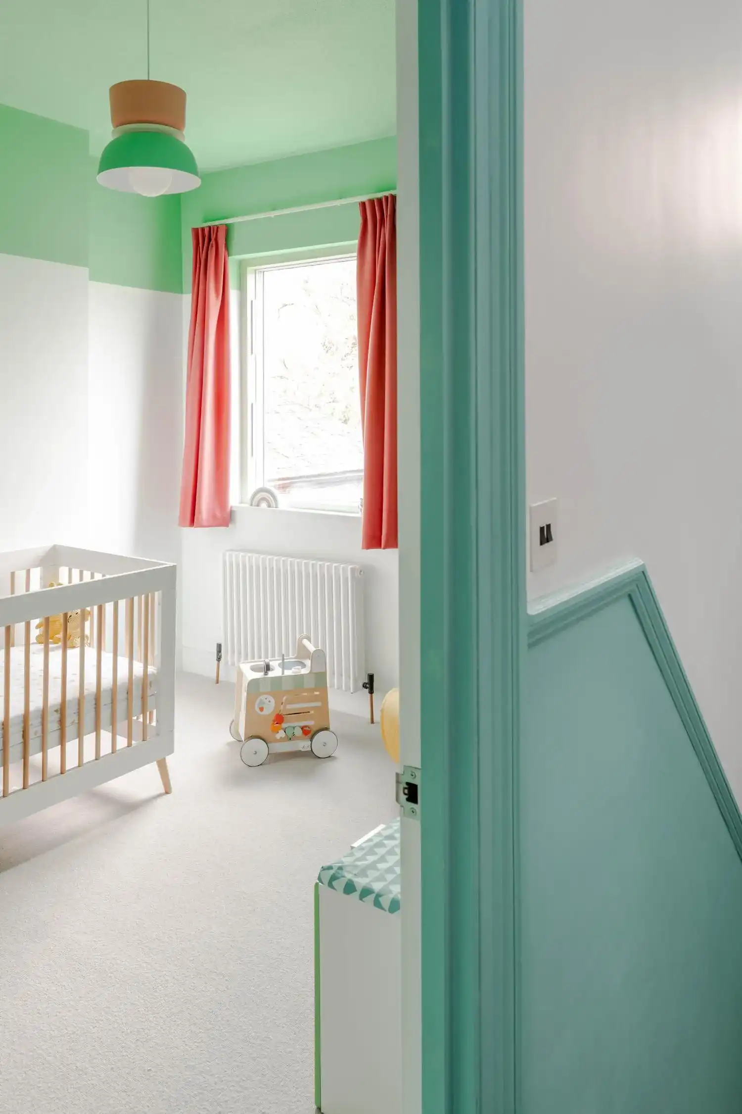 Bright nursery with a white crib, mint green ceiling, and coral-colored curtains.