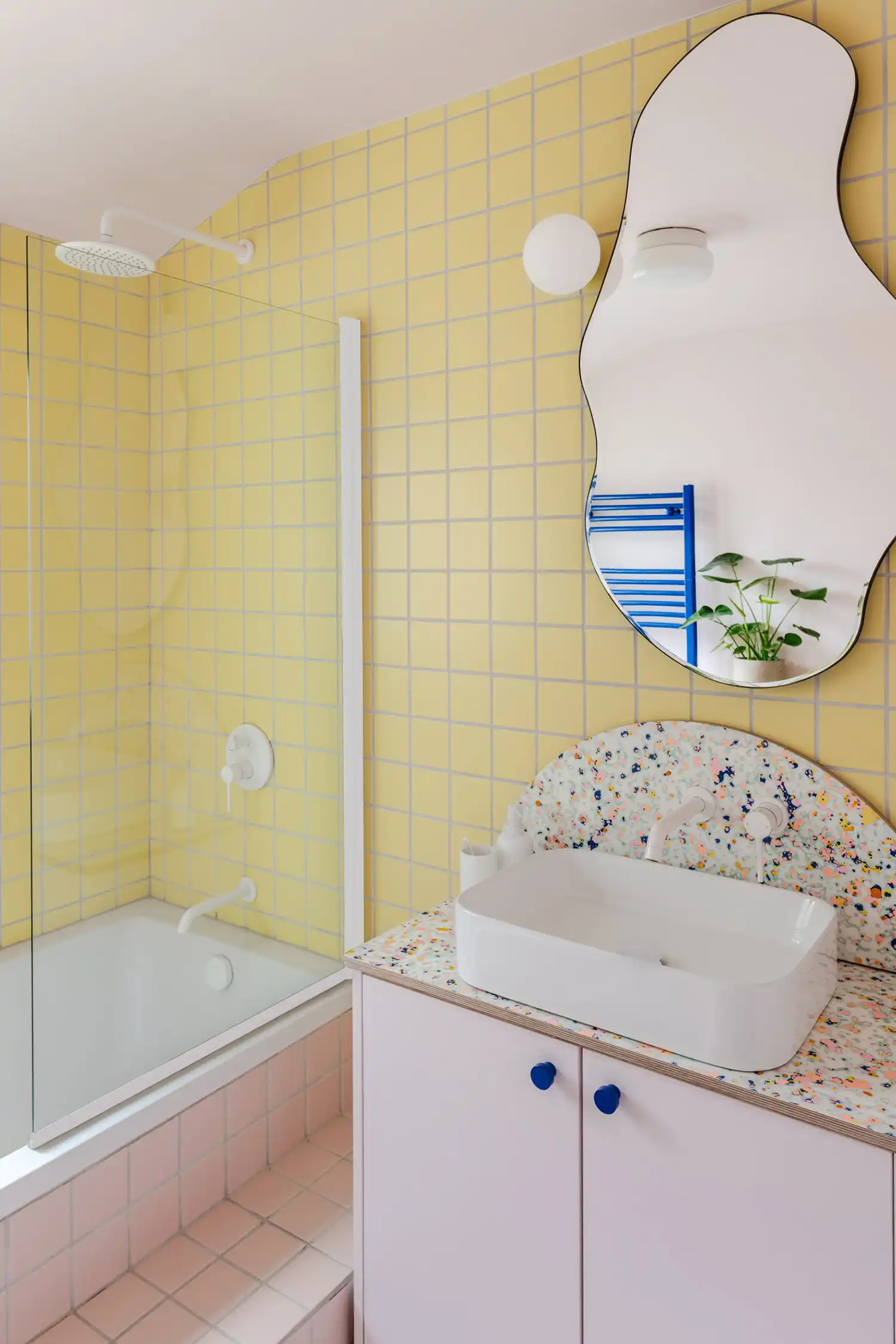 Bathroom with yellow grid tiles, a white rectangular sink on a terrazzo vanity, and an irregular wavy mirror.