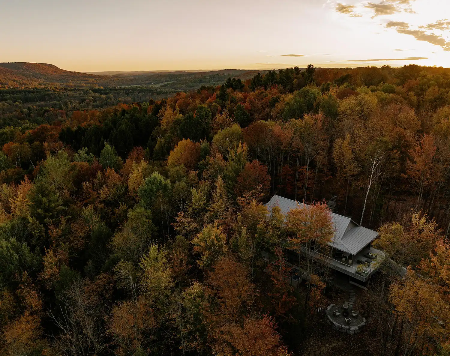 Aerial sunset view of Perchée house submerged in a dense multi-colored forest canopy.