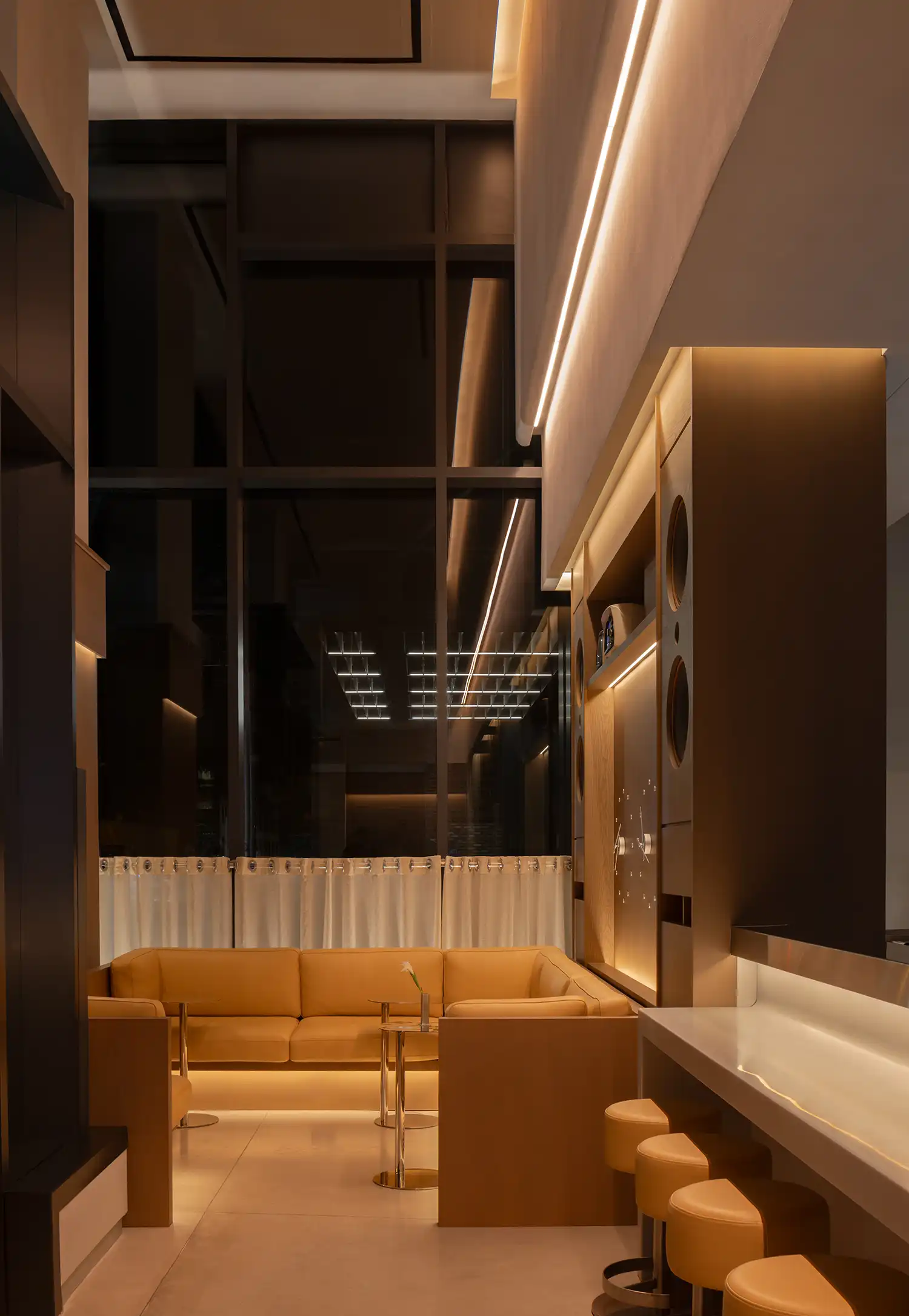 Modern lounge area with tan leather sectional, high ceilings, and warm cove lighting.