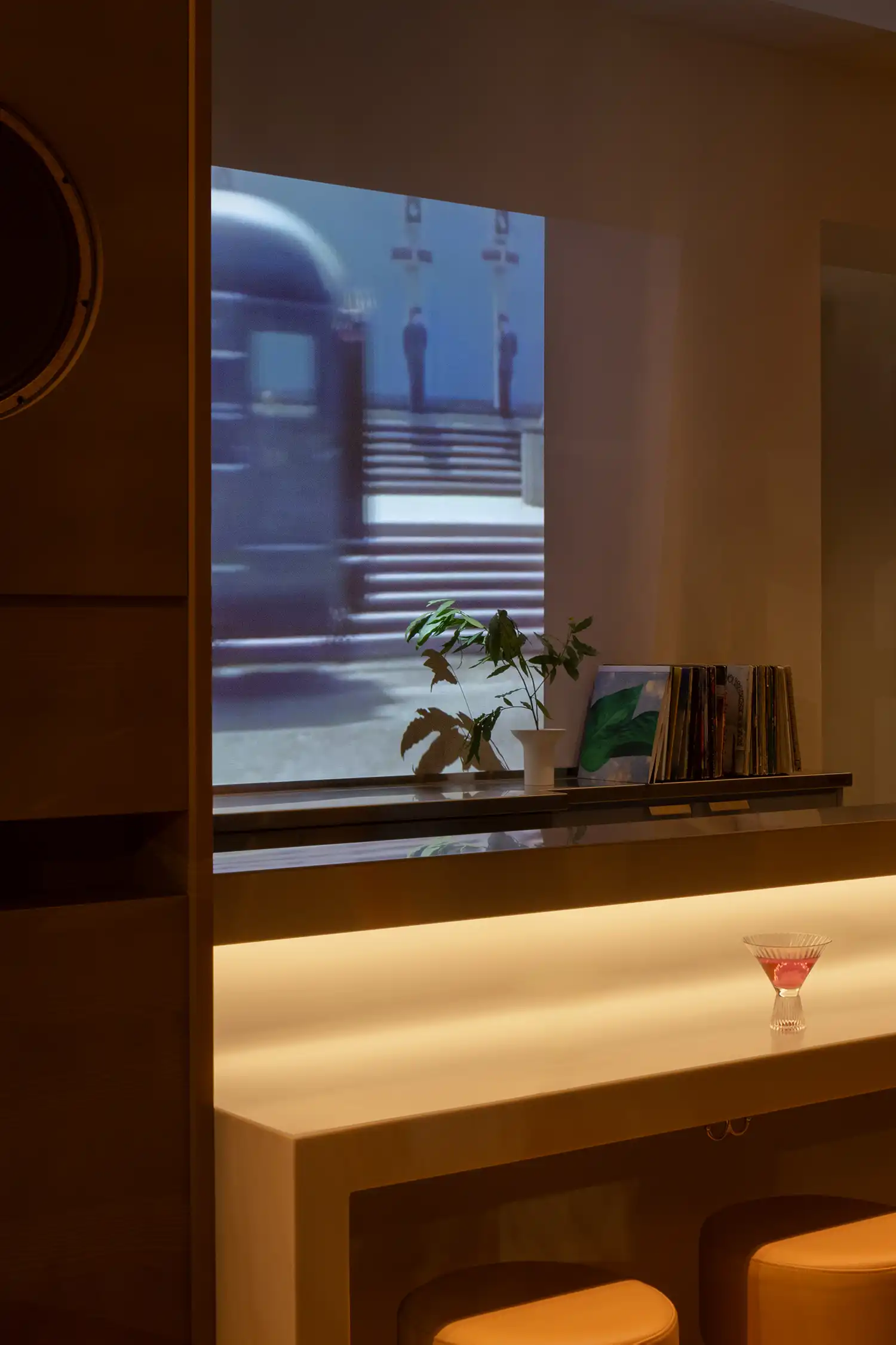Detail of a pink cocktail on a glowing bar counter with projected archival imagery.