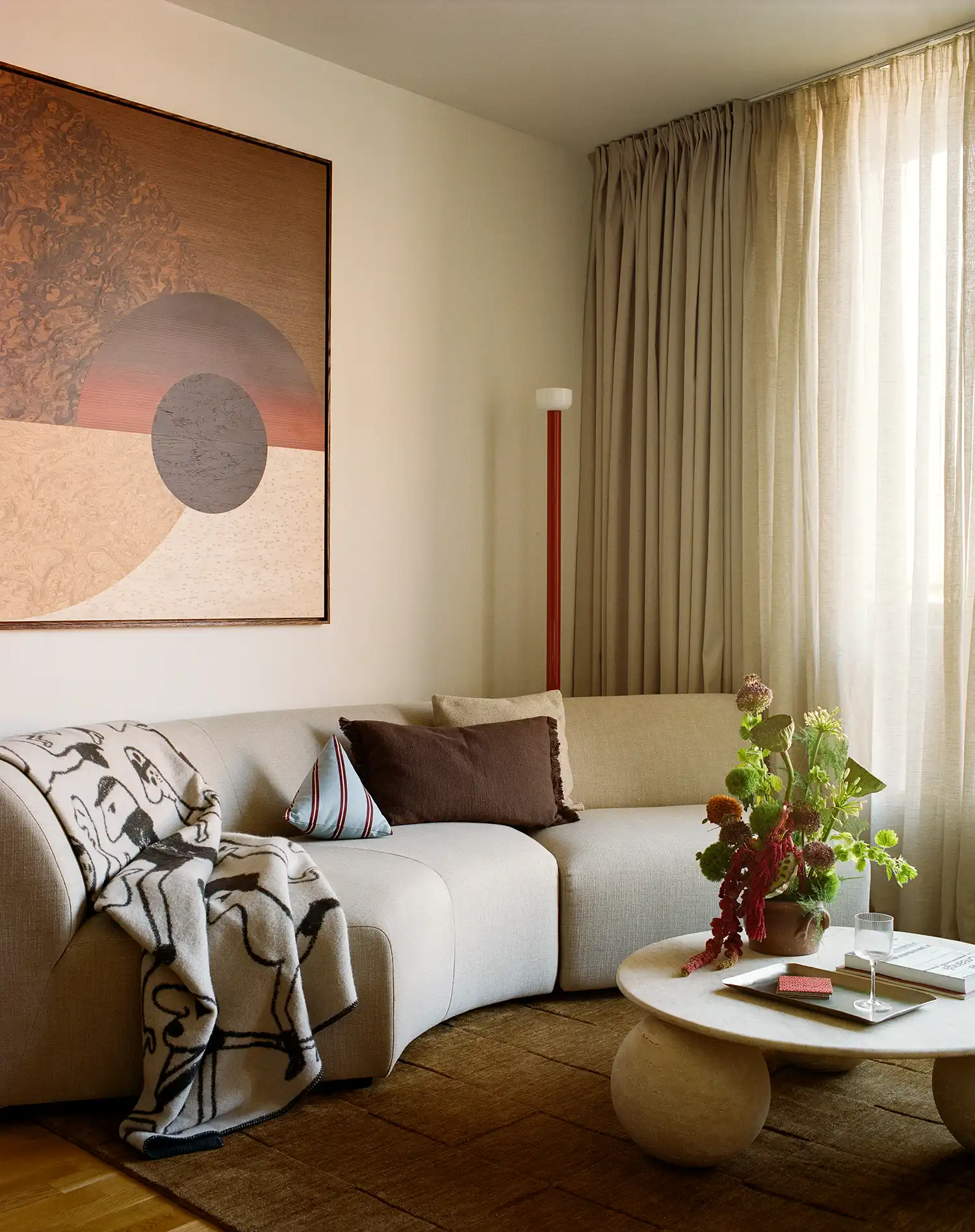 Neutral toned curved sofa with a large abstract marquetry artwork and a decorative wool blanket.