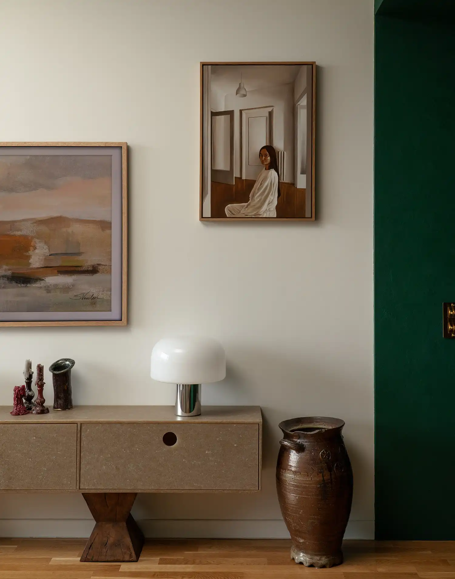 Close-up of a textured sideboard with a white mushroom lamp and two oil paintings on the wall.