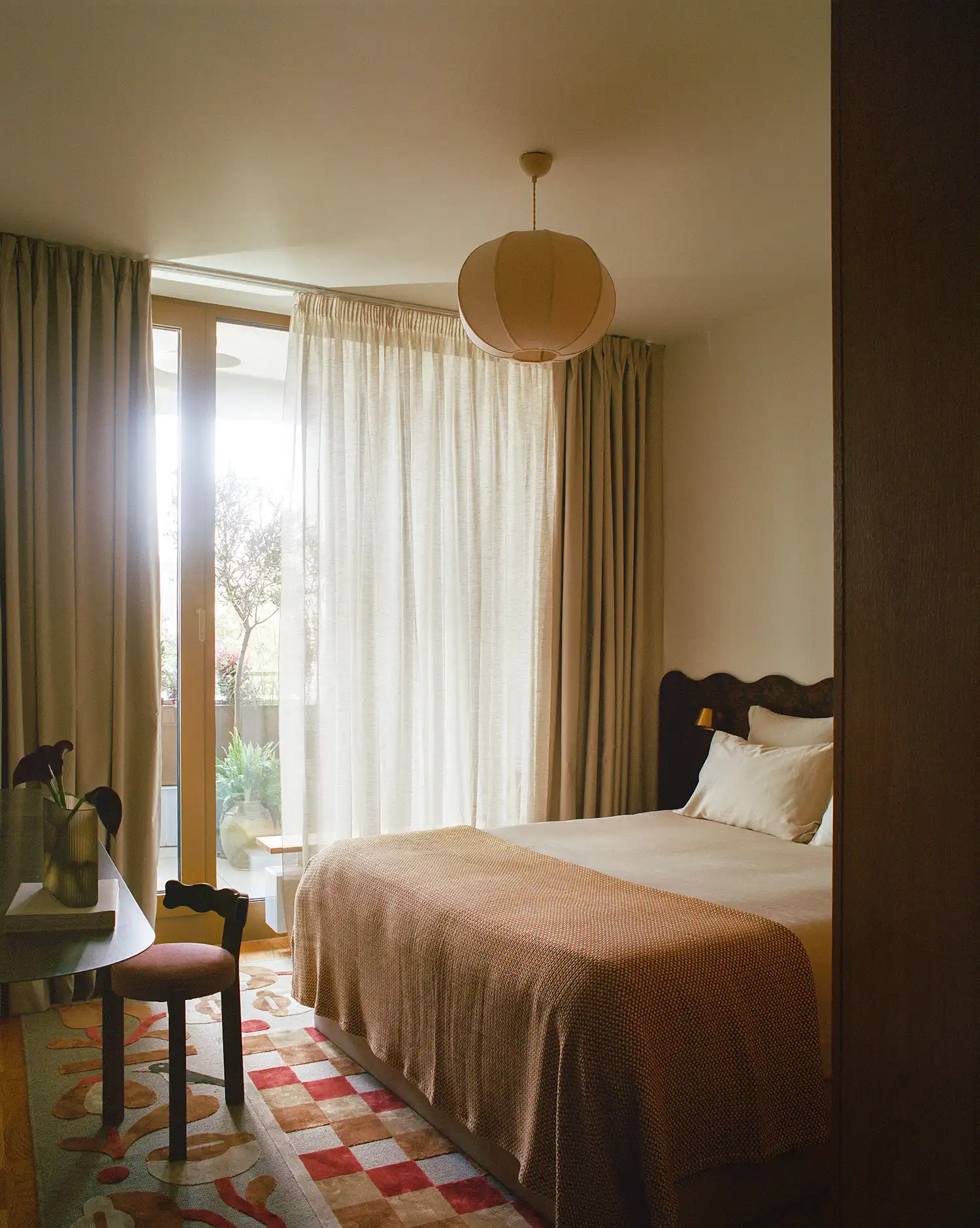 Bright bedroom with a curved headboard, a patterned rug, and a glass door leading to a balcony.