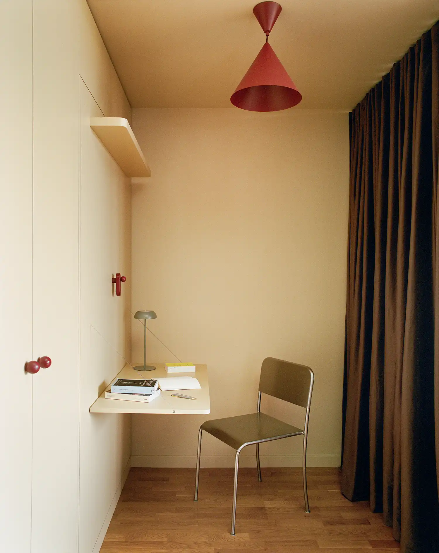 Compact home office nook with a fold-down desk and a red cone pendant light.