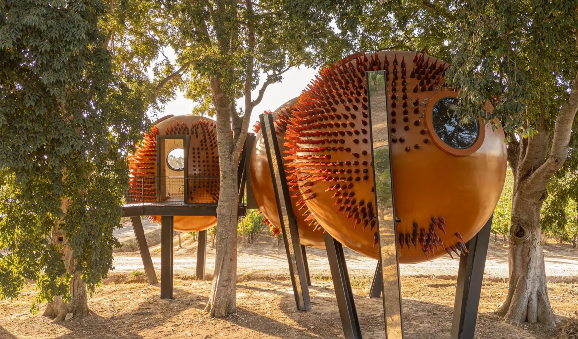 Exterior view of three copper-colored spherical pods supported by black steel pillars among trees.