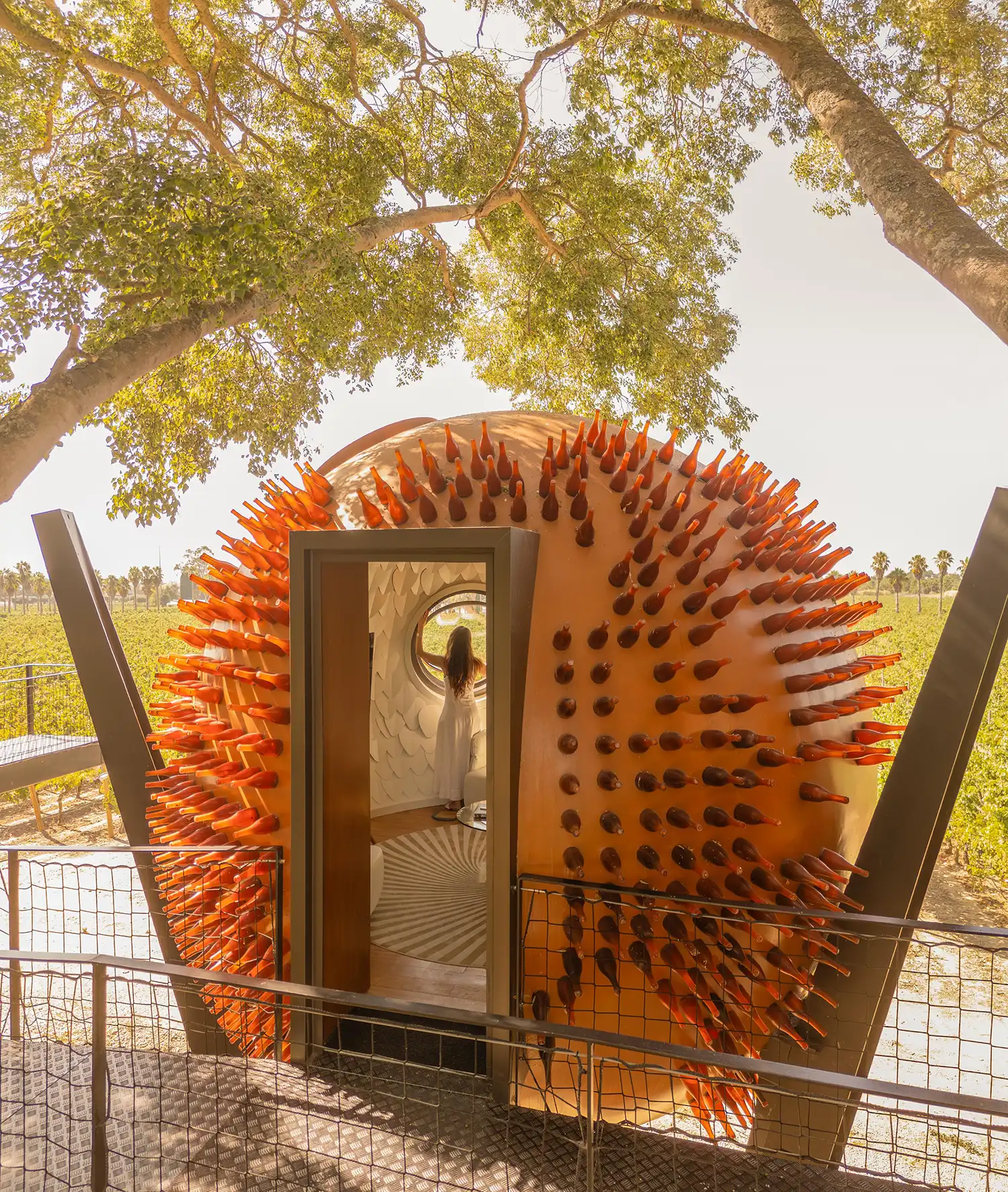 Close-up of a spherical pod entrance showing glass bottle textures and a woman looking through a porthole.
