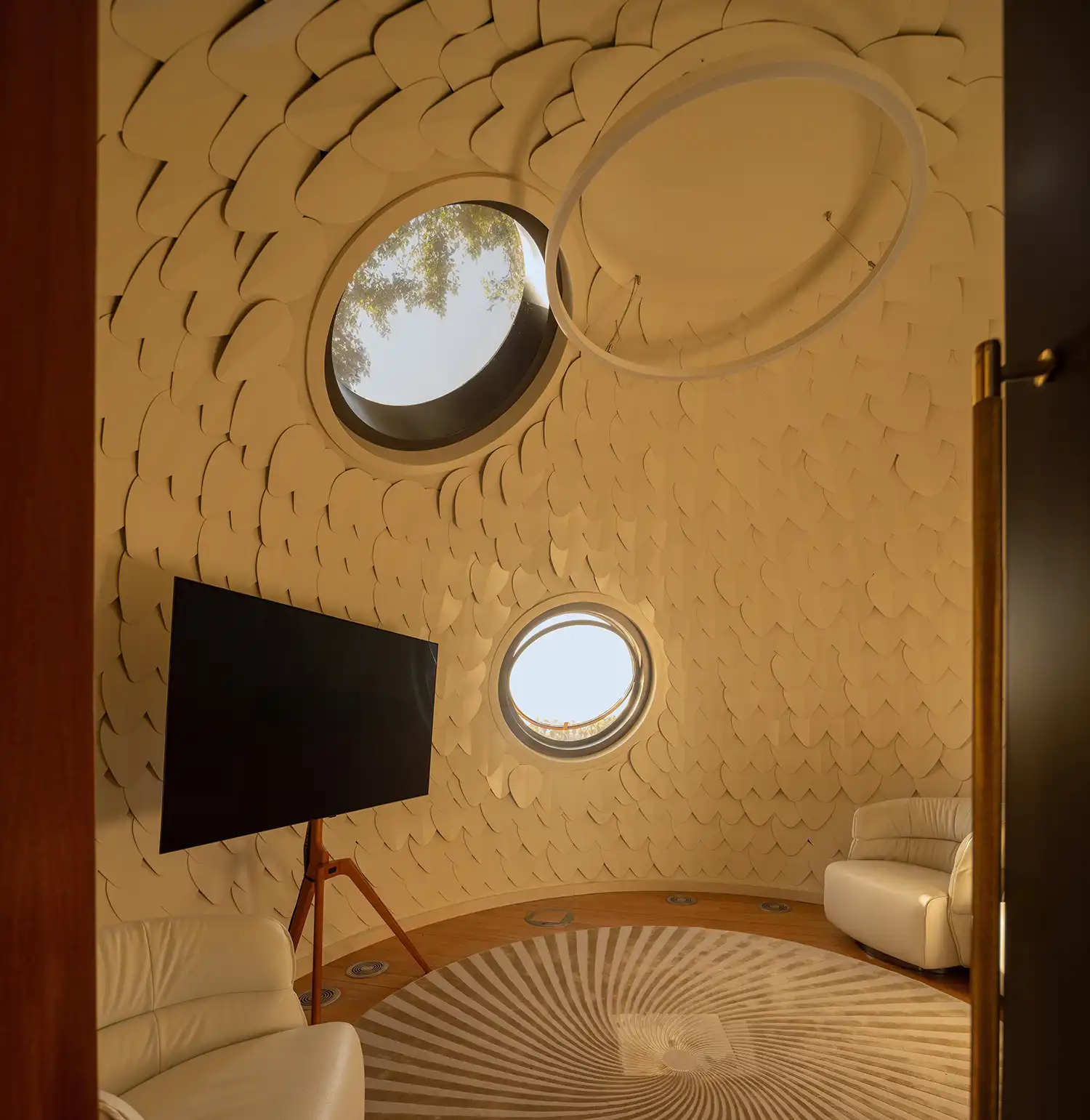 Interior of a white spherical room with leaf-like textured walls, a circular rug, and porthole windows.