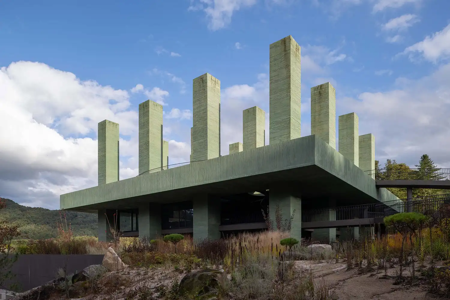 Low angle view of REST restaurant showing tiered concrete strata and wild landscaping