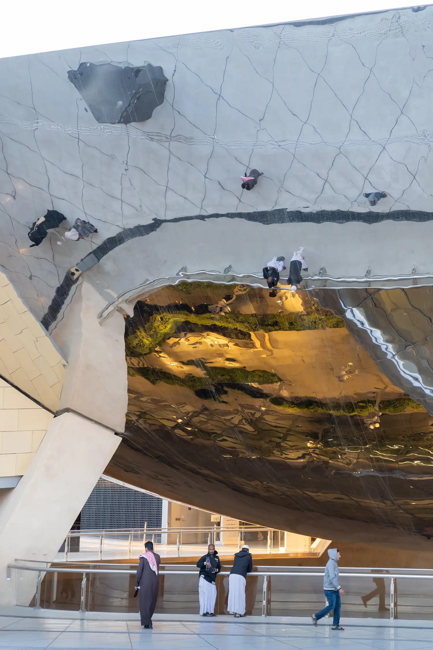 A close-up view from beneath the polished steel canopy, showing the reflection of the plaza and sky above.