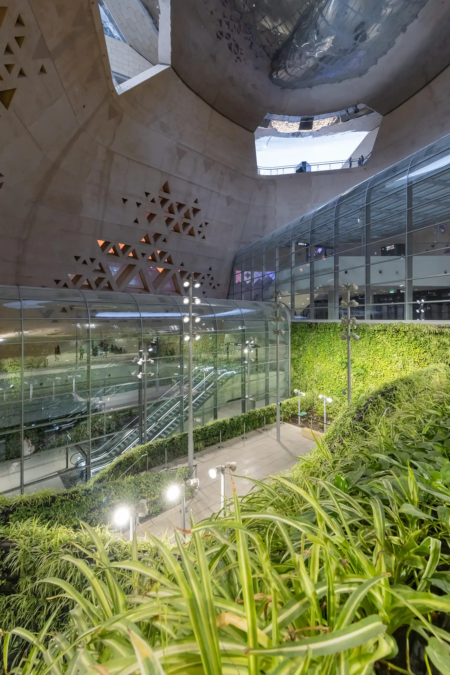 An interior view of the deep atrium featuring a large vertical garden and glass-encased metro platforms.