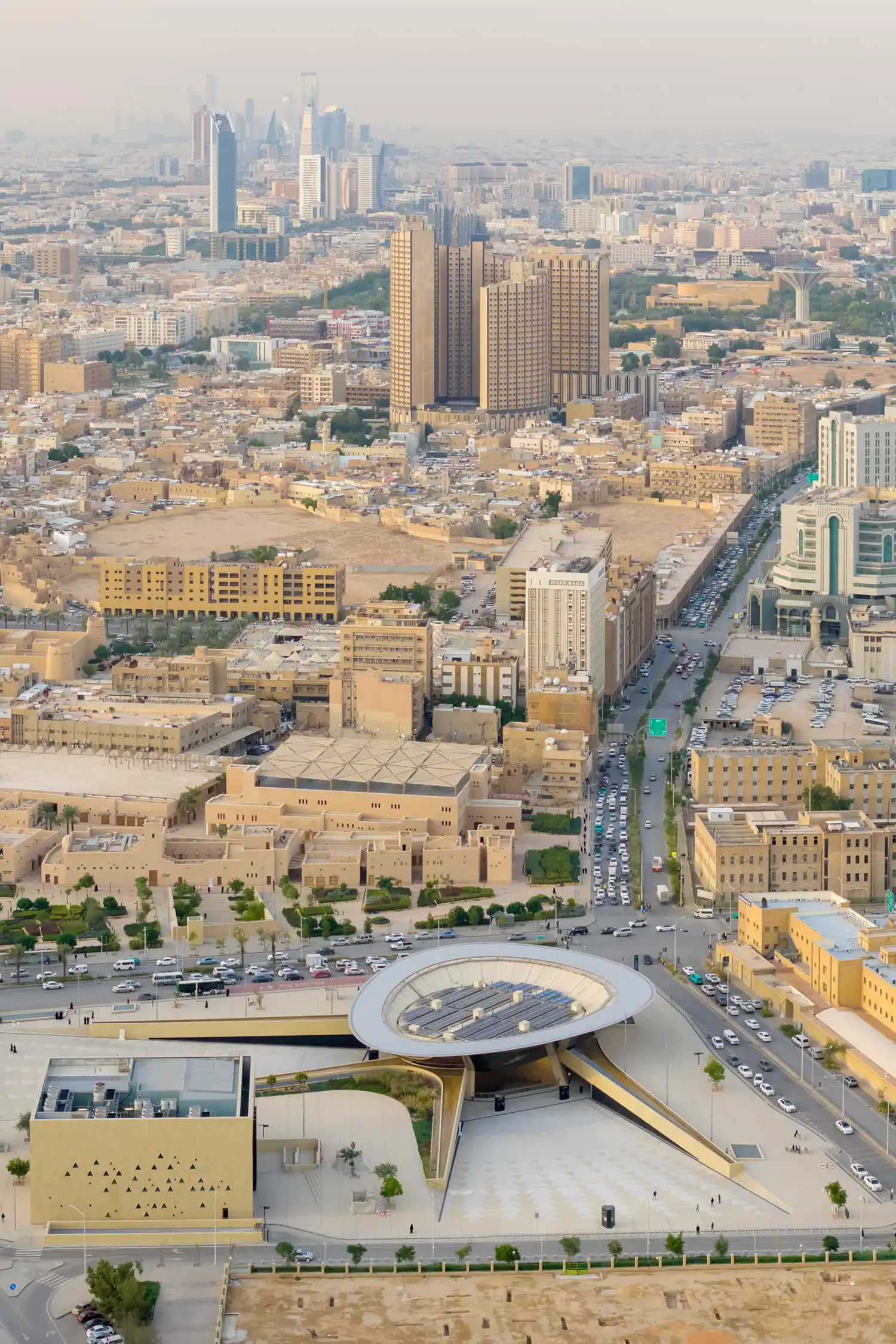 An aerial view of the Qasr Al Hokm Metro Station showing the circular canopy with integrated PV panels amidst the Riyadh city fabric.