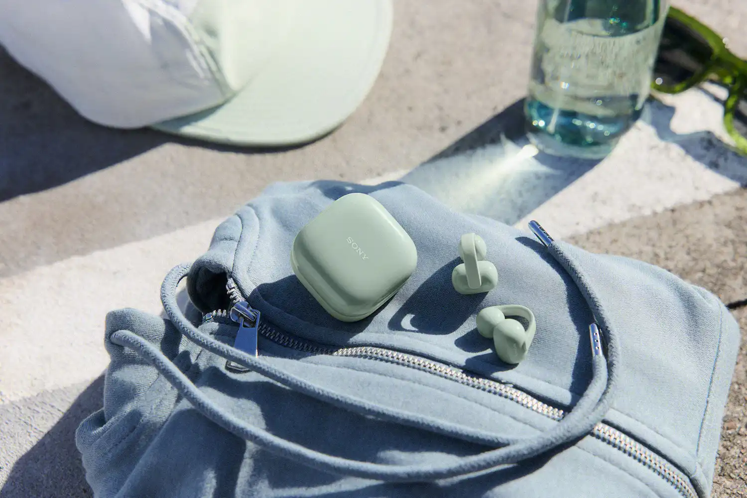 Green Sony LinkBuds Clip and charging case resting on a light blue garment outdoors.