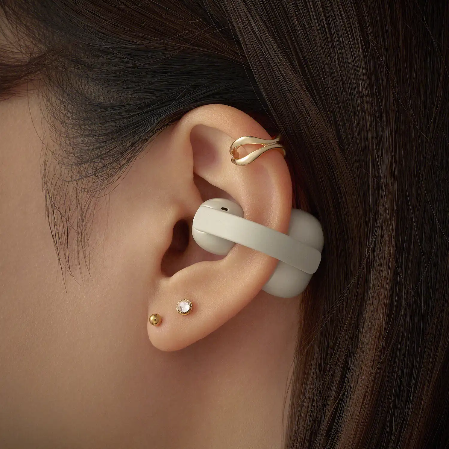 Detailed close-up of the off-white LinkBuds Clip worn alongside a gold ear cuff.