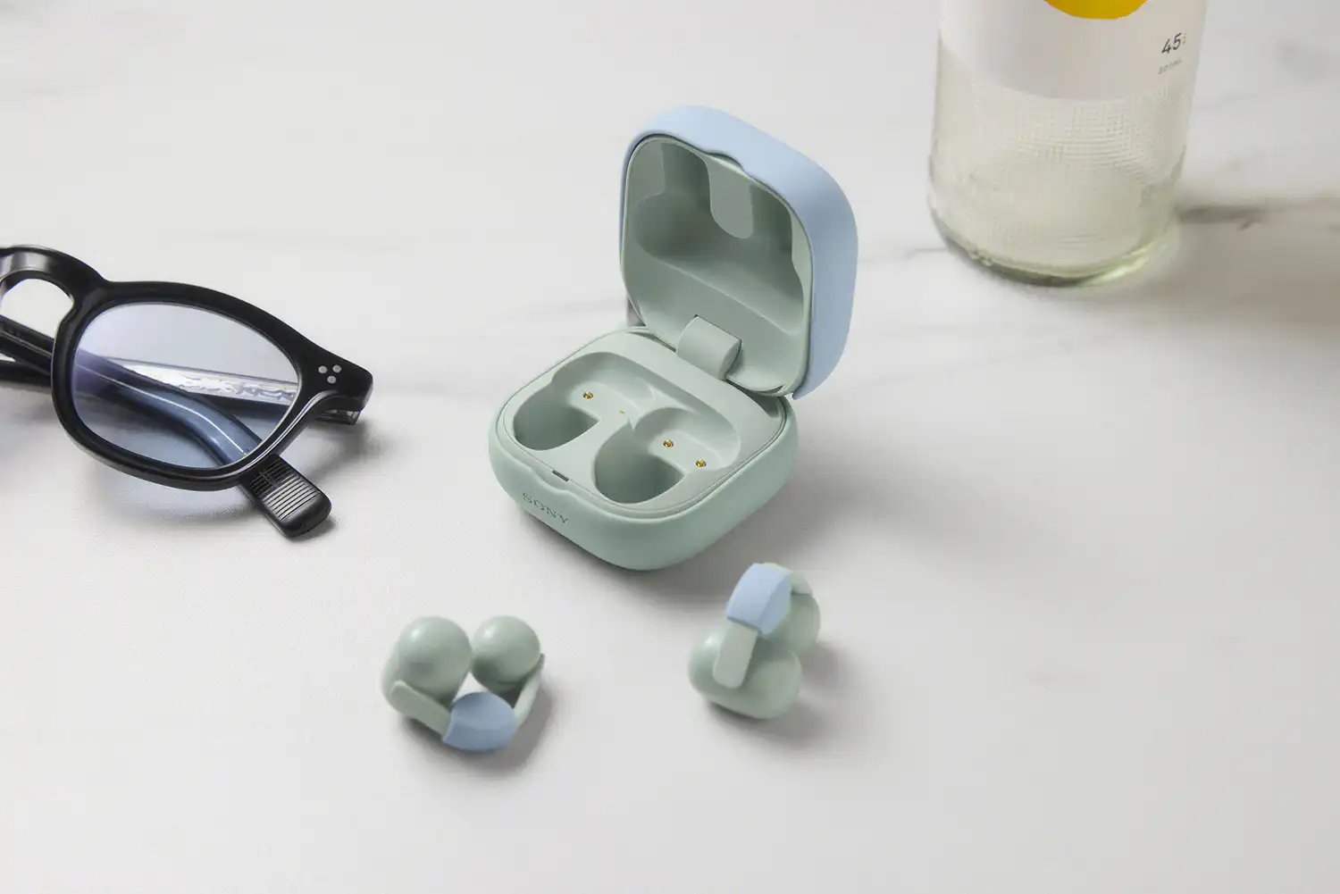 Light green LinkBuds Clip with blue fitting cushions next to an open charging case.