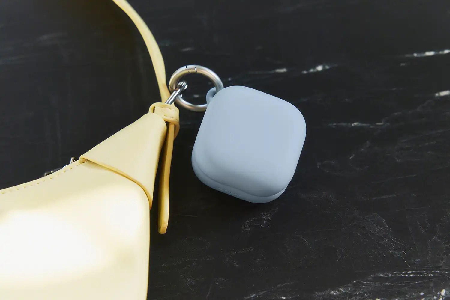 A blue silicone case cover for the LinkBuds Clip attached to a yellow handbag with a metal ring.