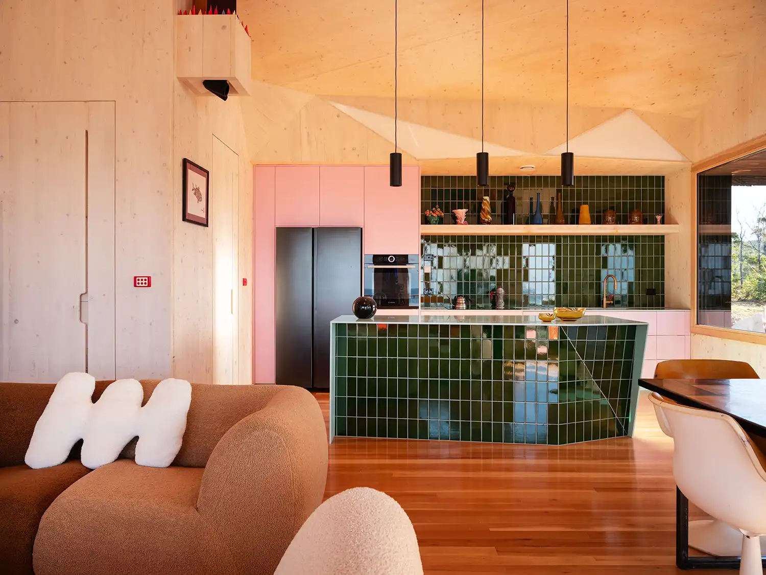 Interior kitchen with a green tiled island and pink cabinets in the Passivhaus kitchen.