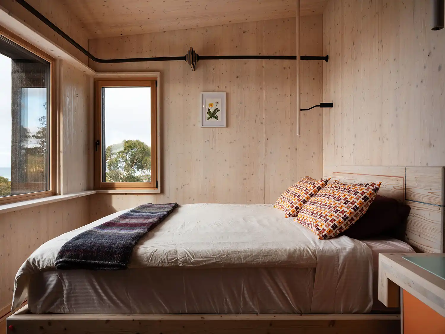 Minimalist bedroom interior with light wood walls and a view of trees from the window.