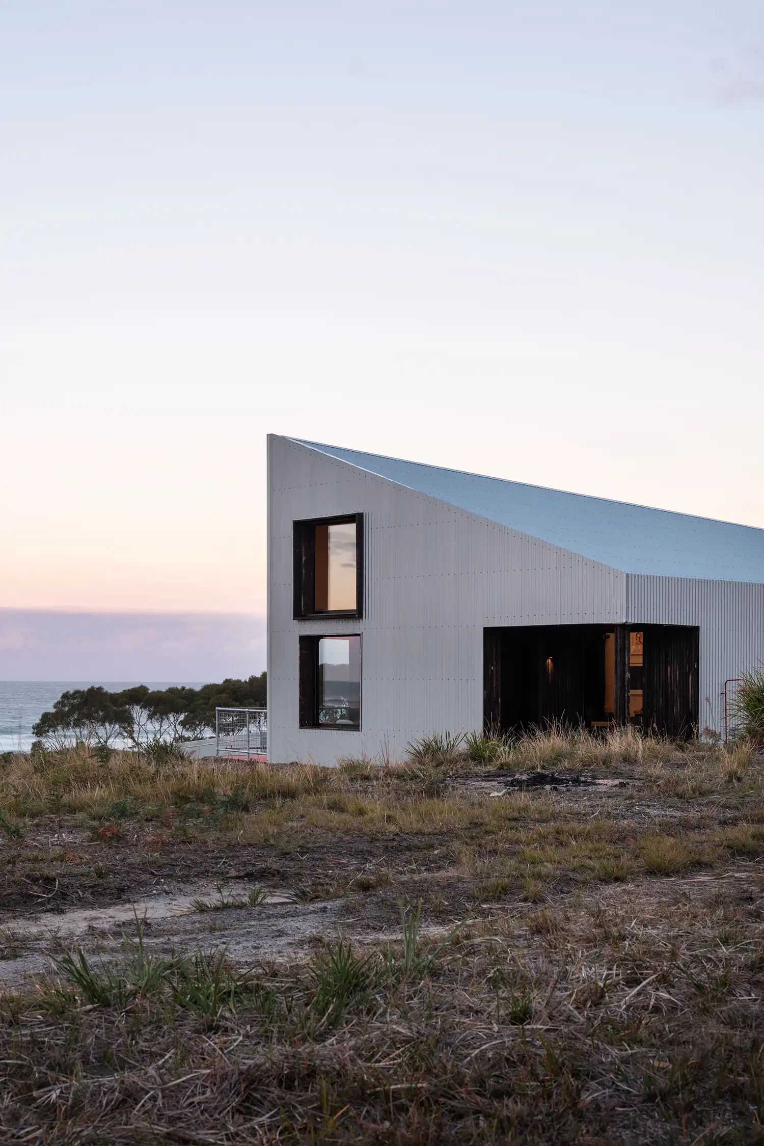 Exterior view of the white metal Passivhaus at dusk overlooking the ocean in Scamander.