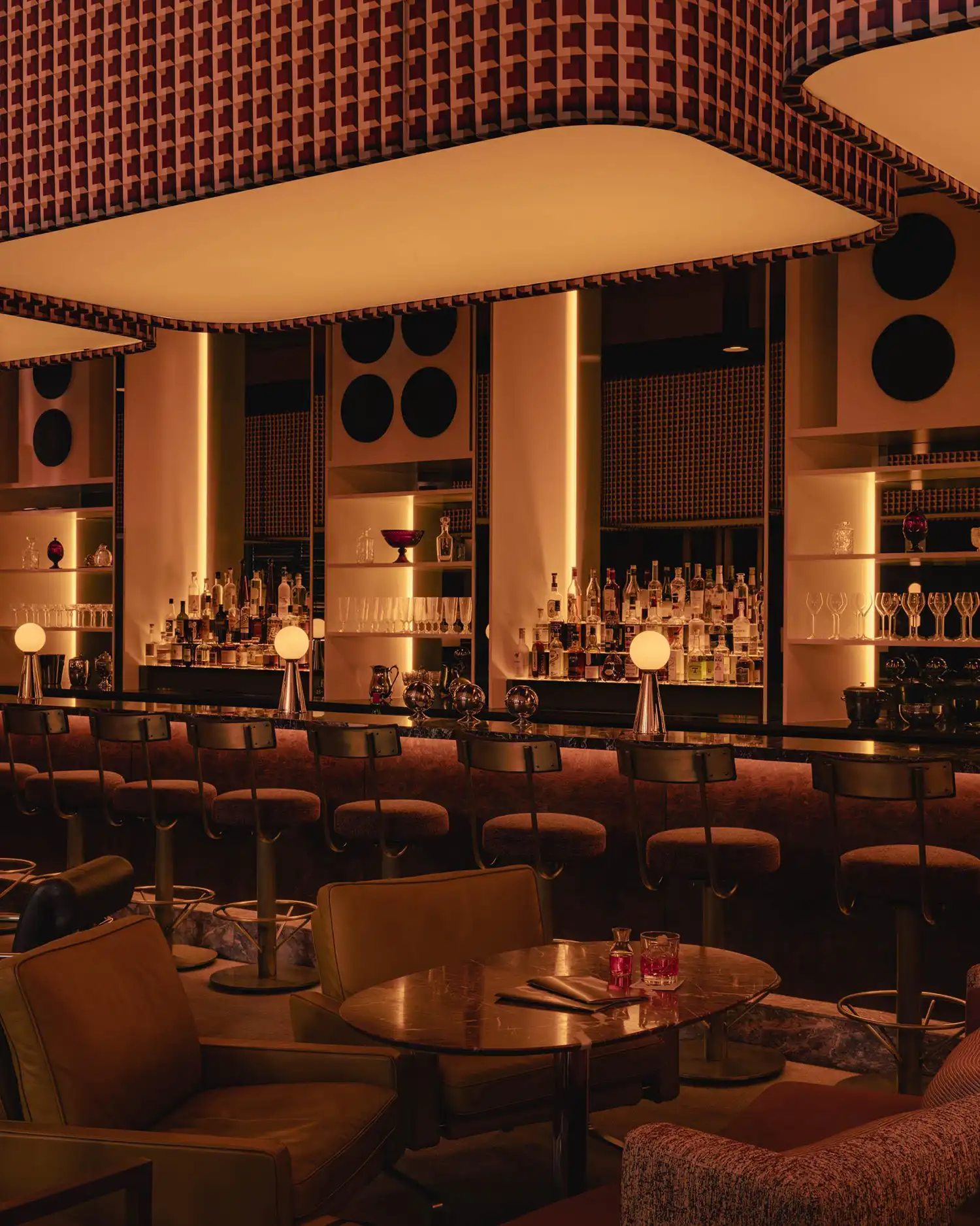 A long bar counter in Mimi featuring Rosso Rubino marble, spherical table lamps, and textured bar stools.