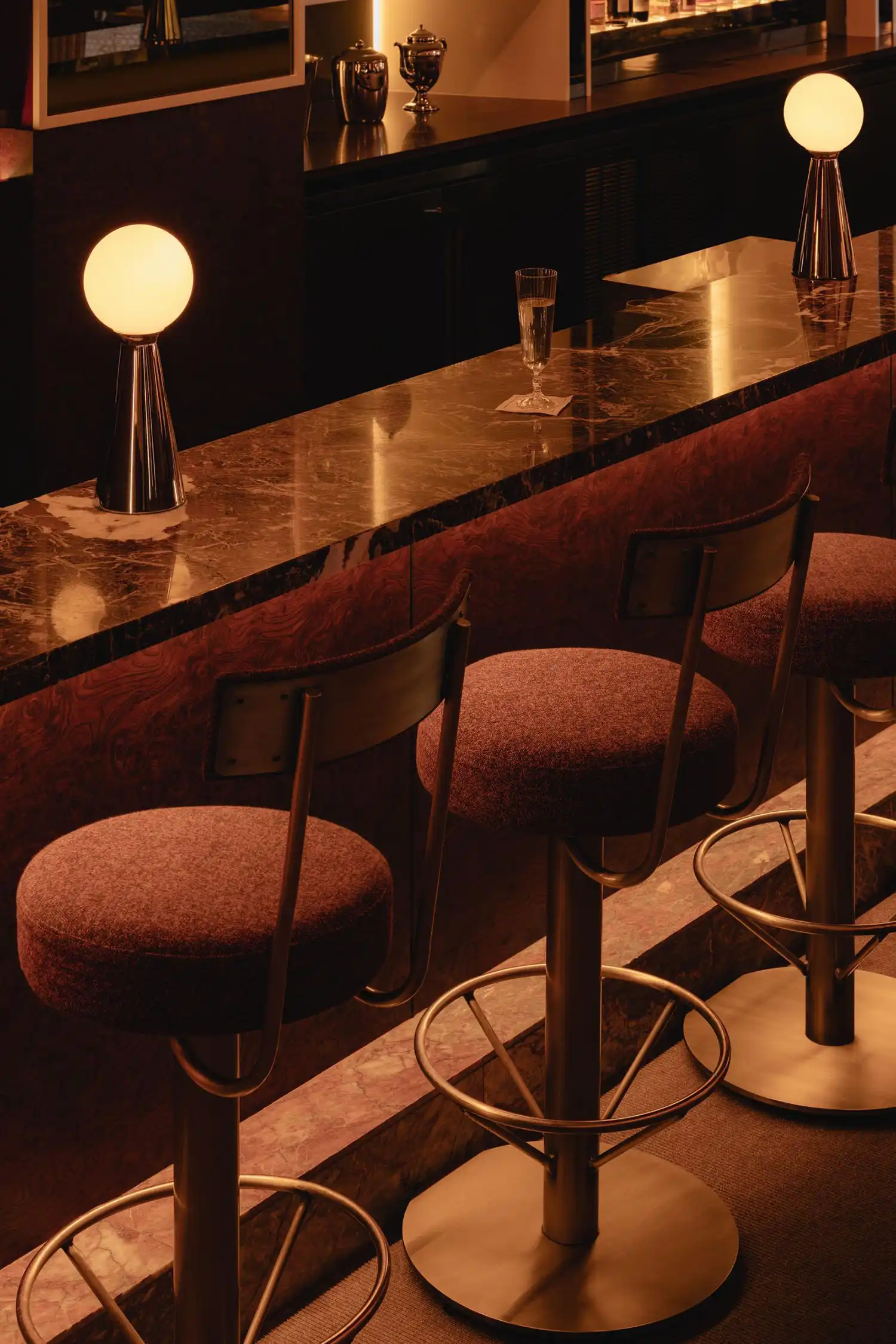 Macro shot of a glass of champagne on a Rosso Rubino marble bar top next to a glowing spherical lamp.