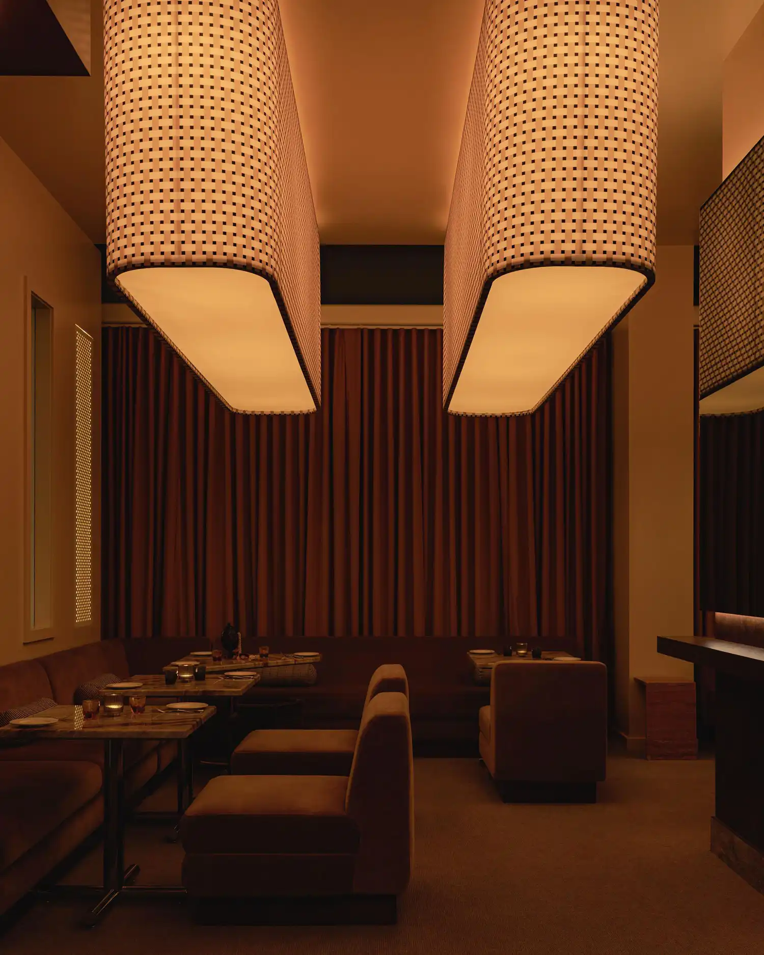 Dining area in Mimi with large capsule pendants featuring woven patterns and floor-to-ceiling drapery.