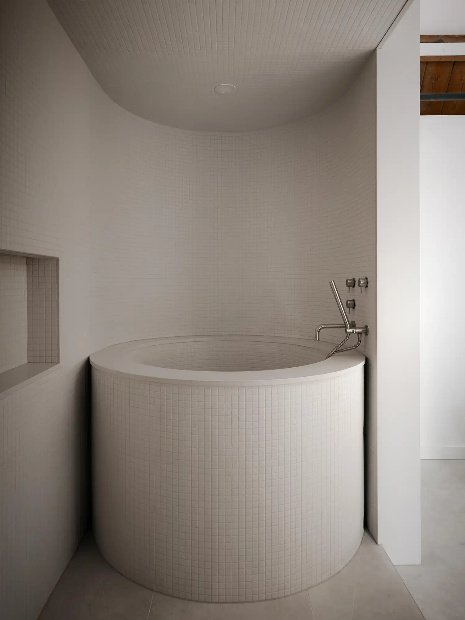 Minimalist circular soaker tub with white mosaic tile detail