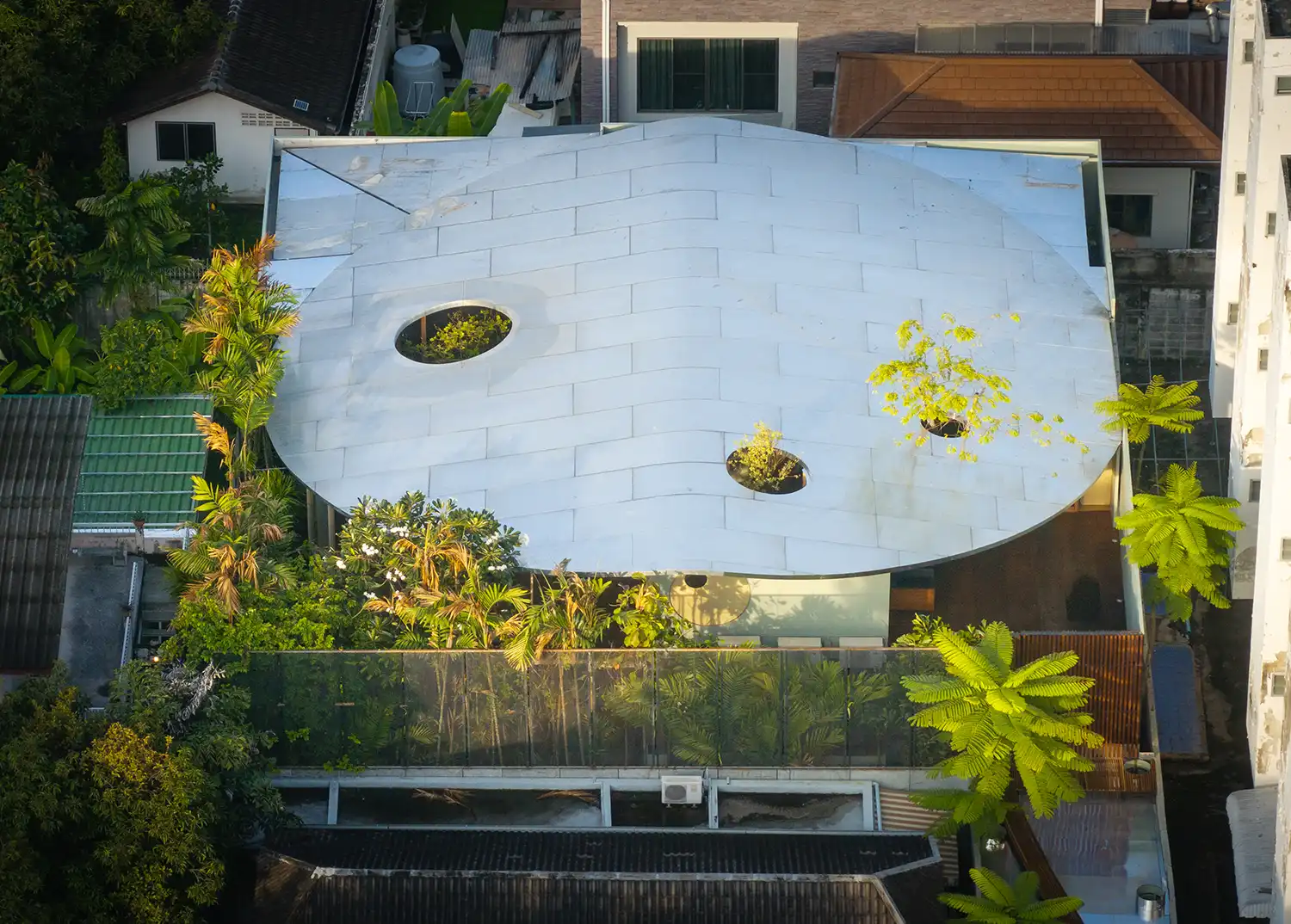 Aerial view of a modern house with a large, white, undulating roof featuring circular cutouts for trees.