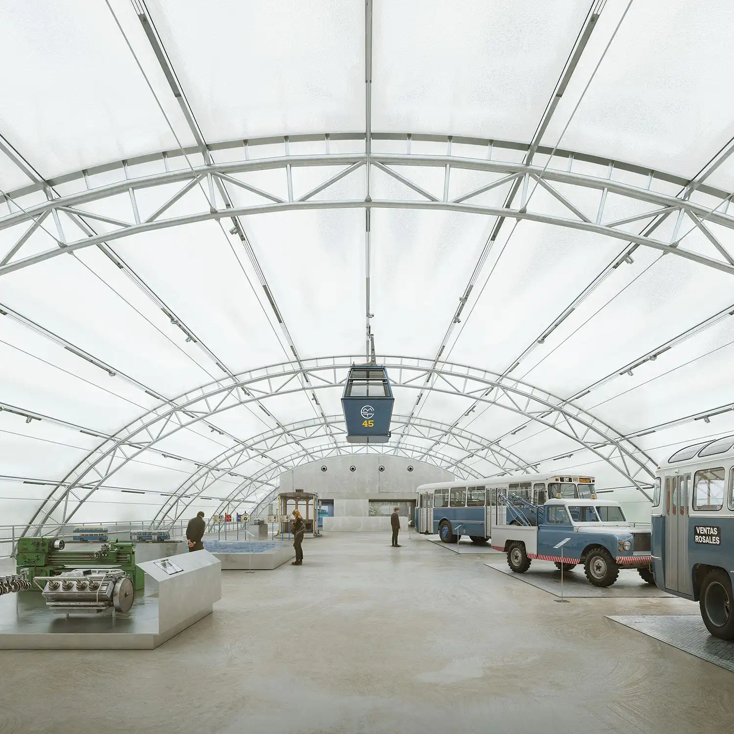 Top floor exhibition gallery showing historic buses and a suspended cable car cabin under the metal arch structure.