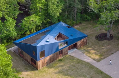 Aerial view of a modern house in Rhode Island with a blue metal roof and solar panels next to a river.
