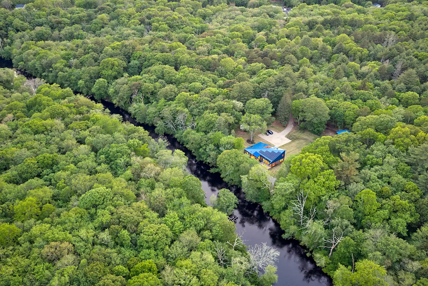 Aerial shot of the Riverhouse surrounded by lush green forest and a river.
