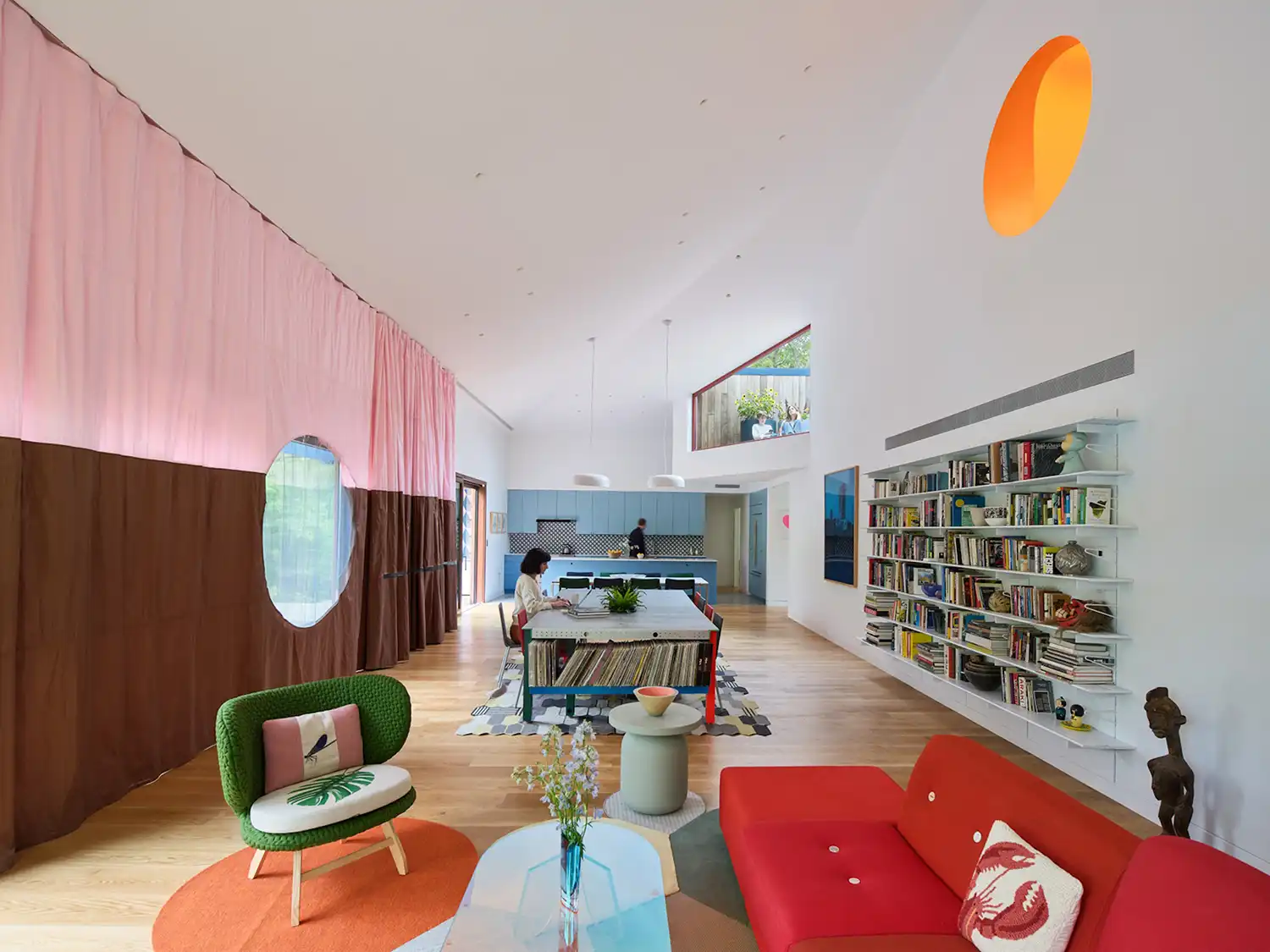 Interior view of a long, white living room with a large dining table and vibrant furniture.
