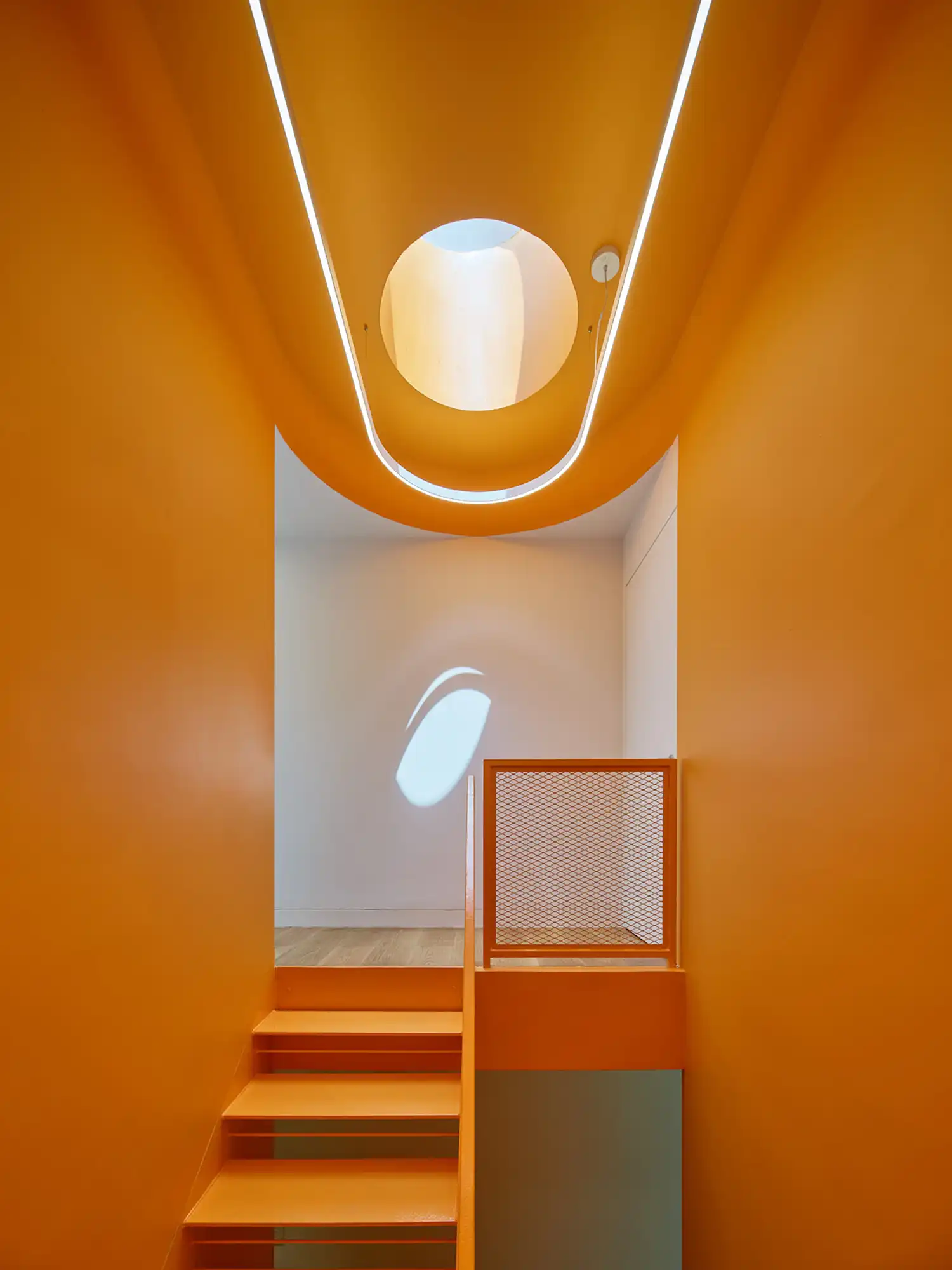 Modern staircase painted in vibrant orange with a circular skylight above.